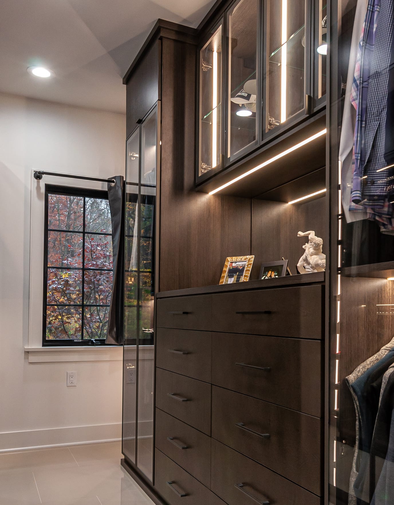His portion of the couple's master walk in closet in dark wood finish with built in dresser by California Closets
