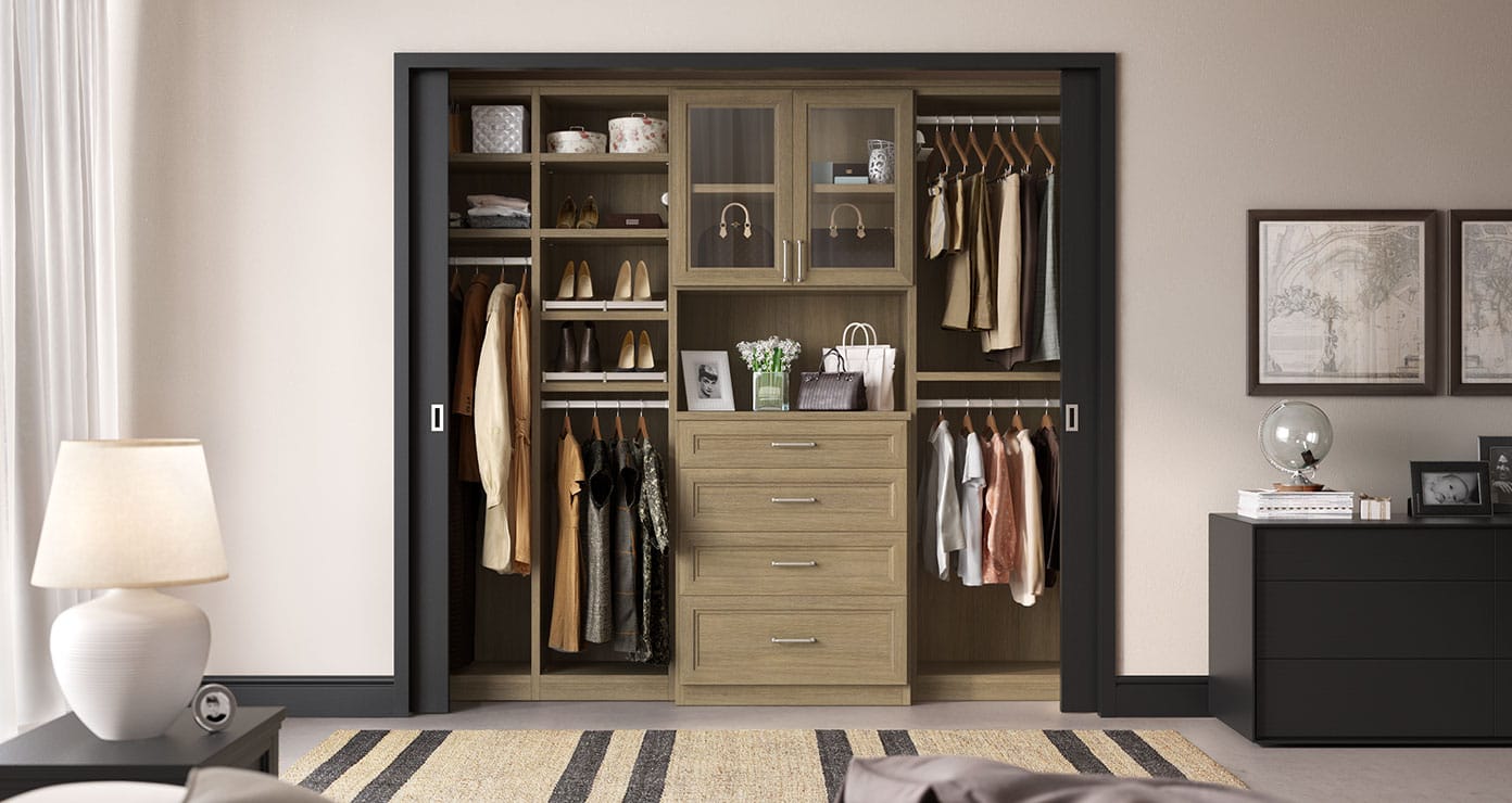 Custom reach in closet with built in dresser, glass door cabinets in walnut finish by California Closets